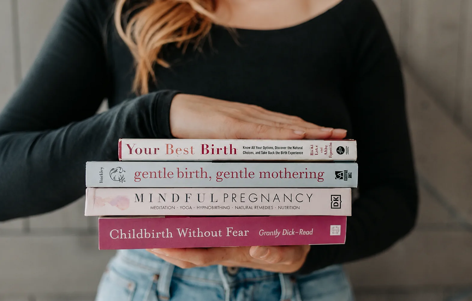 A person holding a stack of pregnancy and childbirth books.